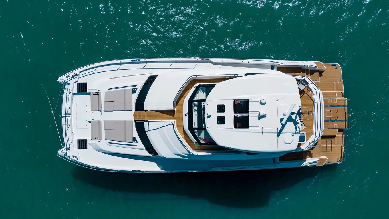 Aerial view of a luxurious yacht with sun loungers and wooden decking, floating on clear turquoise waters.